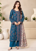 A woman models a long teal blue printed kurta with red and gold border details, paired with matching teal wide-leg pants in a styled indoor setting with beige walls and white vases.