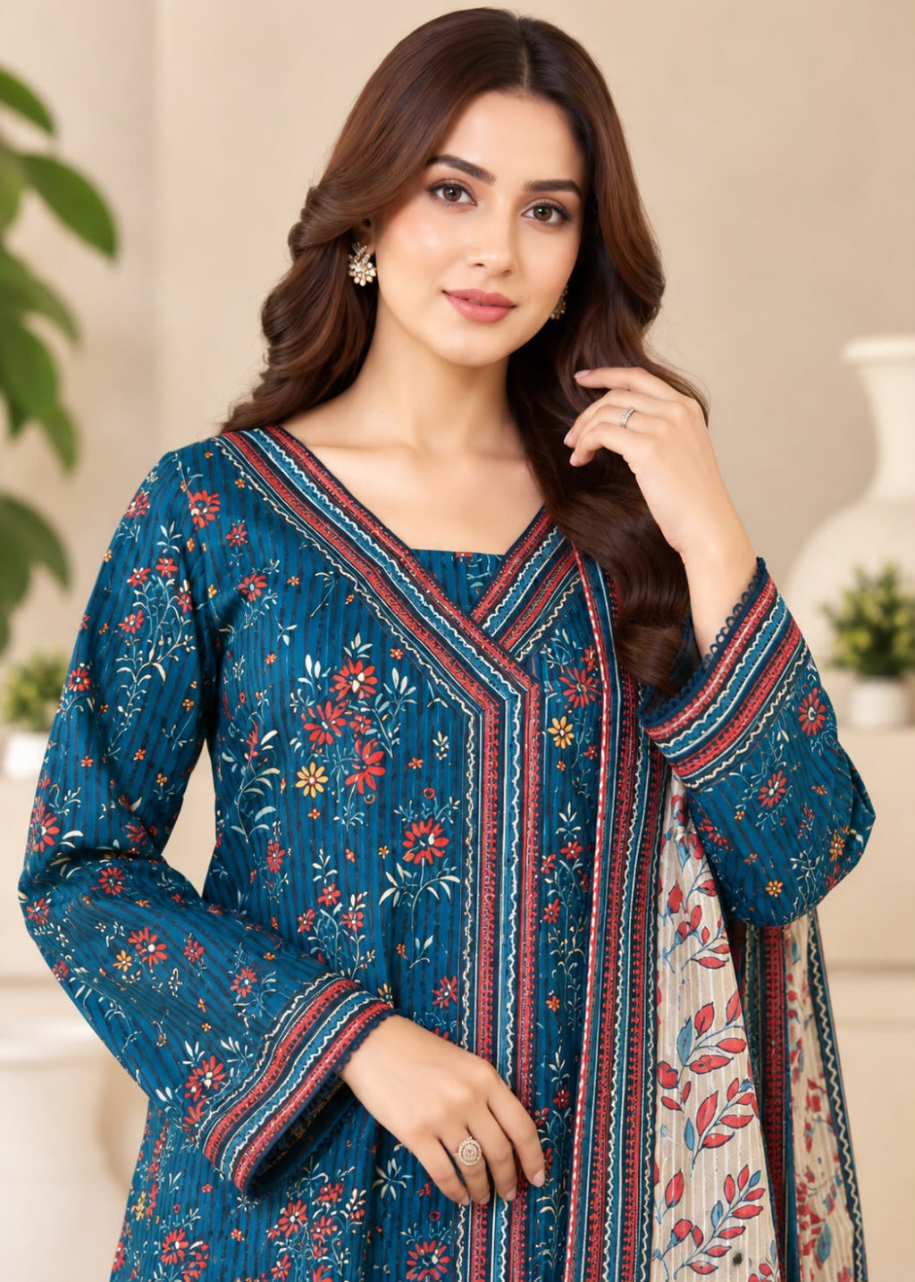 A woman modeling a teal blue ethnic salwar kameez set with red and gold floral embroidery and a matching dupatta, set against a softly blurred indoor background.