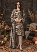 A woman stands in a rustic autumn setting wearing a beige and black zebra-print kurta with a matching printed dupatta, paired with light beige pants and beige flats. The background features a dark wooden wall, pumpkins, and dry grass.