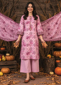 A woman stands in a styled autumn scene wearing a pink printed kurta with matching wide-leg pants and a draped dupatta. The setting includes pumpkins, logs, dried grass, and scattered leaves on the ground.