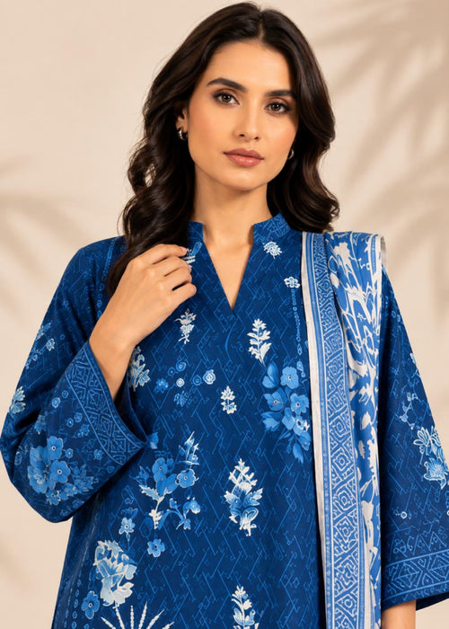 A woman wearing a royal blue embroidered kurta with white floral patterns and a matching patterned dupatta, set against a warm beige background with soft leaf shadows.
