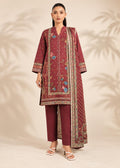 A woman models a three-piece traditional outfit consisting of a maroon kurta with colorful floral embroidery, matching maroon trousers, and a coordinating embroidered dupatta, set against a warm beige background with soft palm leaf shadows.