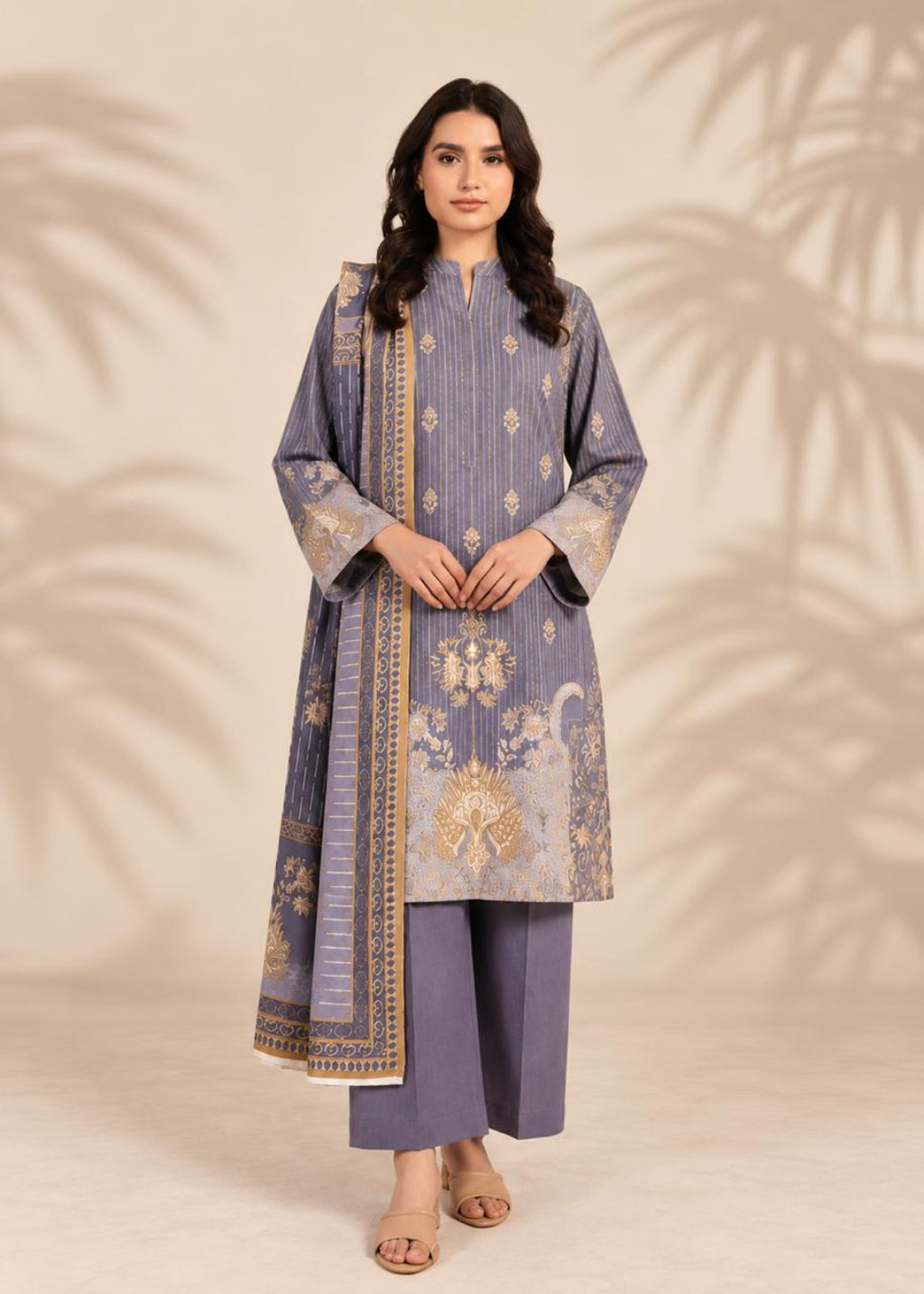 A woman modeling a traditional three-piece salwar kameez suit in dusty lavender with gold and beige embroidery, set against a warm beige background with soft palm leaf shadows.