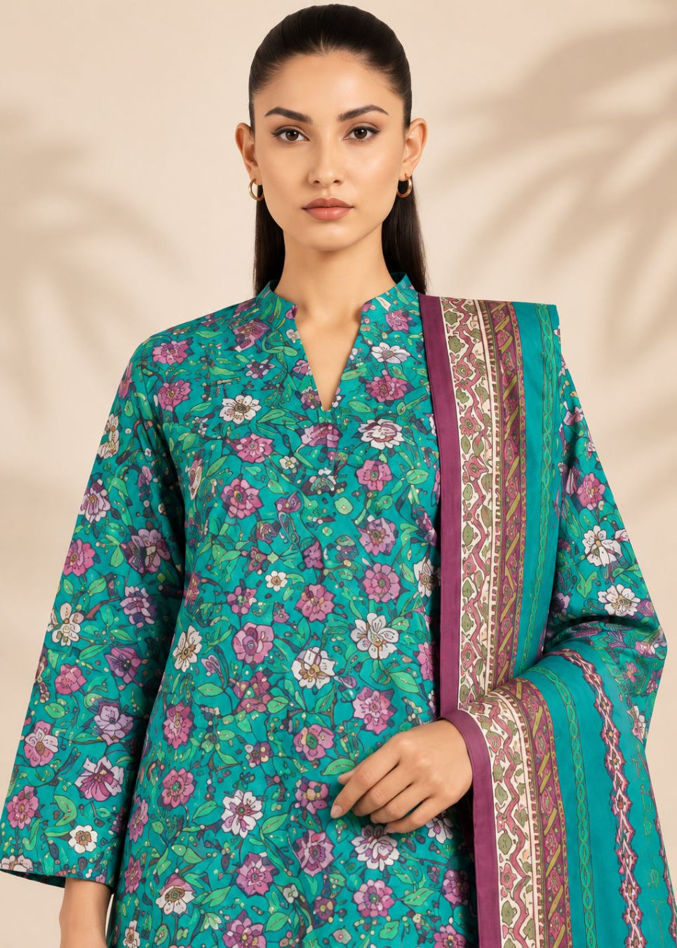 A woman modeling a teal green floral printed kurta with a matching patterned dupatta, set against a warm beige background with soft leaf shadows.