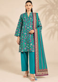 A woman models a traditional three-piece salwar kameez suit set. The set features a teal green kurta with a colorful floral print, matching teal green trousers, and a coordinating teal green dupatta with a detailed purple and gold border.