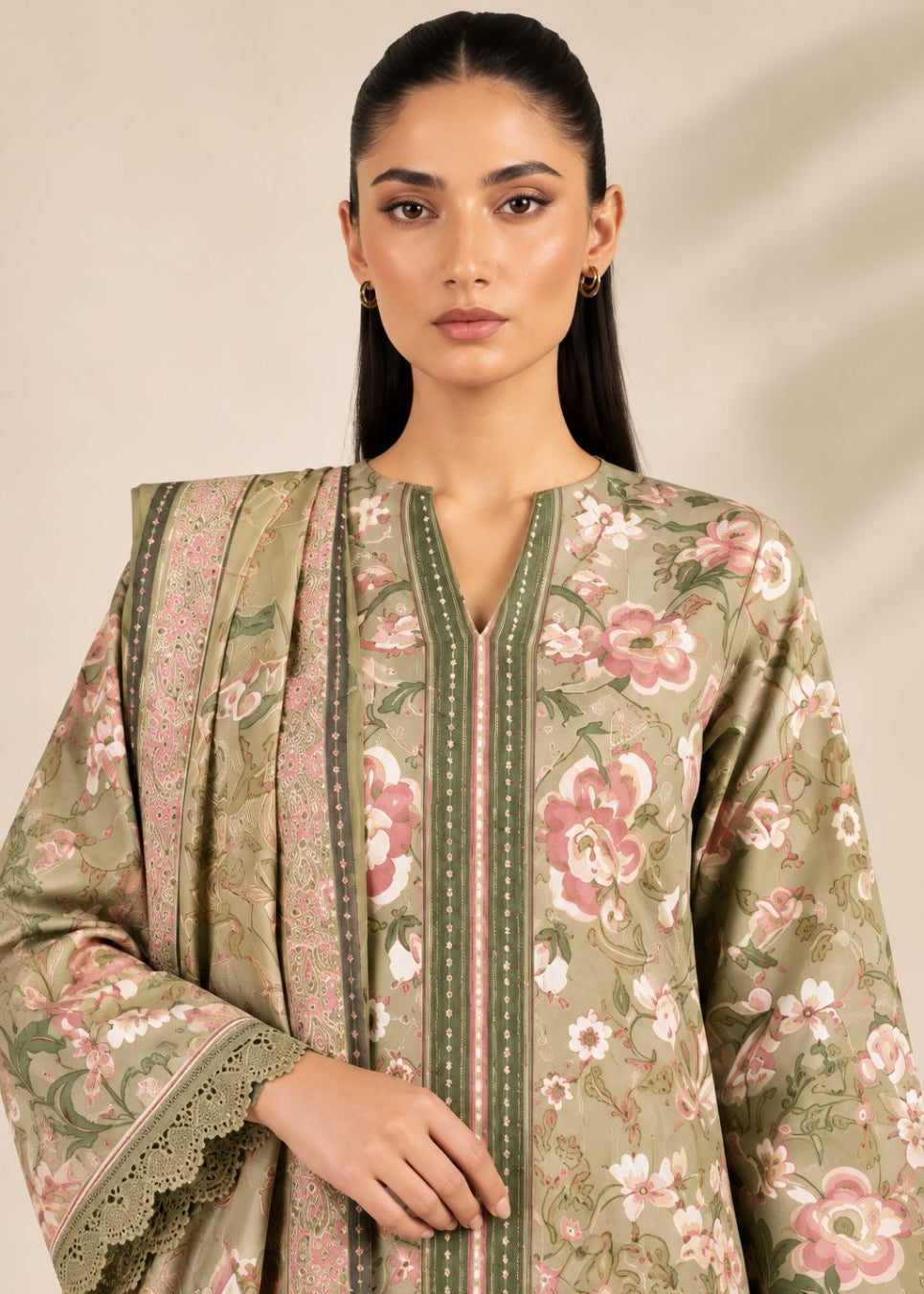 A woman modeling a traditional three-piece salwar kameez suit in sage green with pink and white floral prints, featuring a matching dupatta.