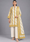 A woman modeling a traditional three-piece salwar kameez suit set. The set features a cream-colored kurta with intricate gold and green floral patterns and gold borders, paired with matching cream wide-leg trousers and a coordinating dupatta.
