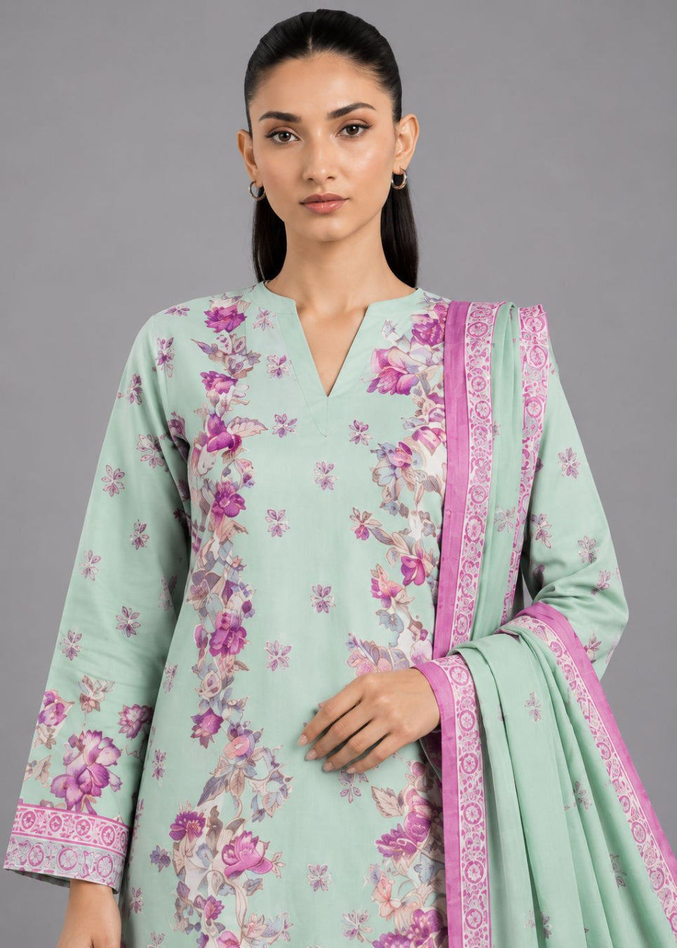 A woman modeling a mint green salwar kameez suit with a pink floral print and a matching pink border dupatta, set against a solid gray studio background.