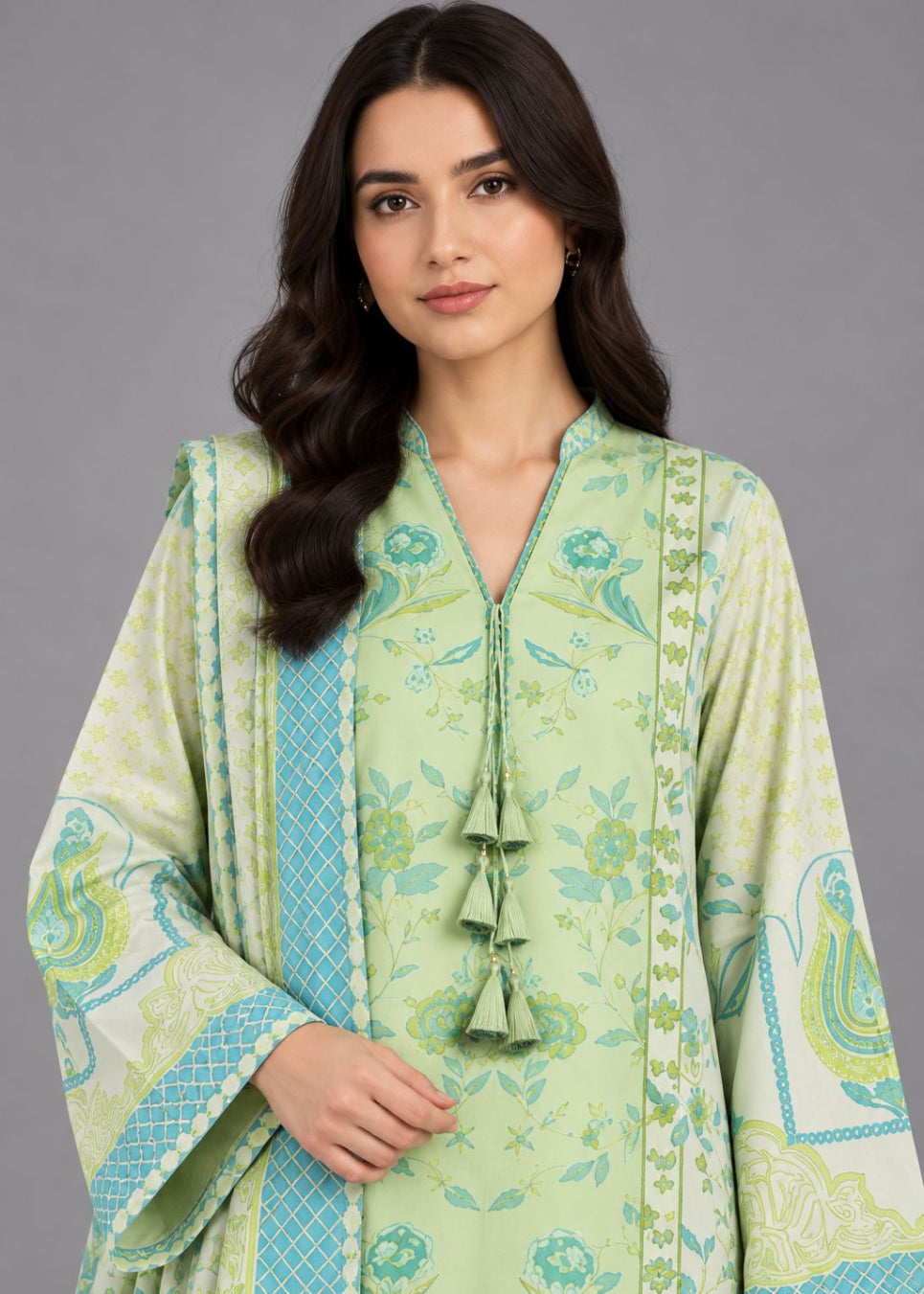 A woman modeling a light green traditional kurta with blue and white floral patterns, tassel tie, and wide sleeves against a solid gray background.