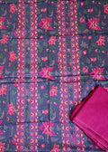 A folded dark navy fabric with pink and magenta floral patterns and vertical printed stripes, displayed on a green artificial turf surface with other packaged fabrics around it. A matching folded magenta fabric piece is placed on the lower right.