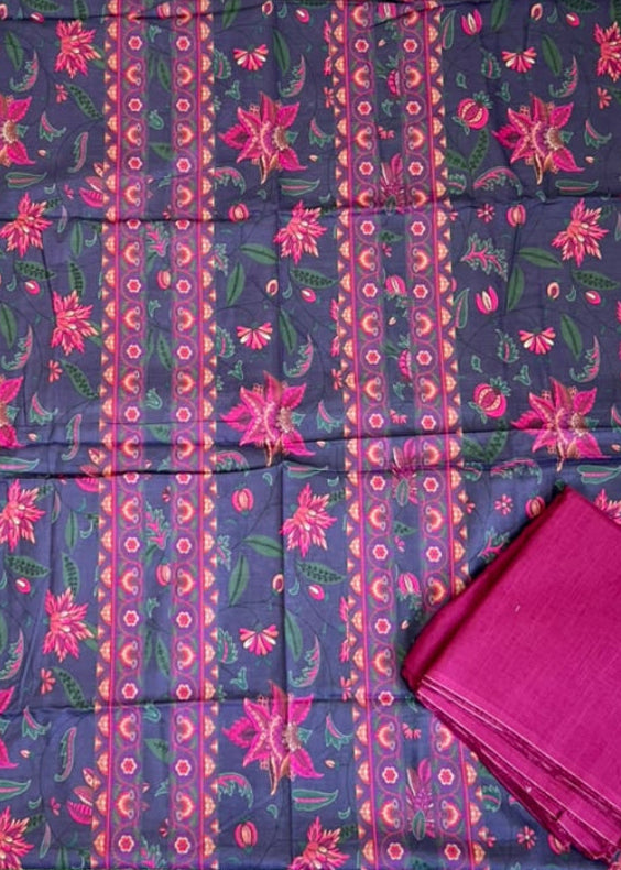 A folded dark navy fabric with pink and magenta floral patterns and vertical printed stripes, displayed on a green artificial turf surface with other packaged fabrics around it. A matching folded magenta fabric piece is placed on the lower right.