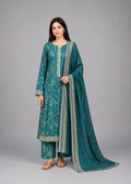A woman modeling a teal green ethnic three-piece suit with beige floral embroidery and a matching dupatta, set against a solid gray studio background.