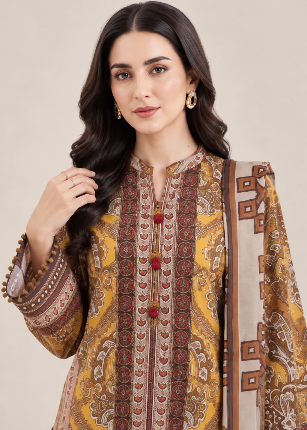 A woman modeling a traditional South Asian salwar kameez set featuring a mustard yellow and brown paisley patterned kurta with red decorative accents, paired with a matching beige dupatta.