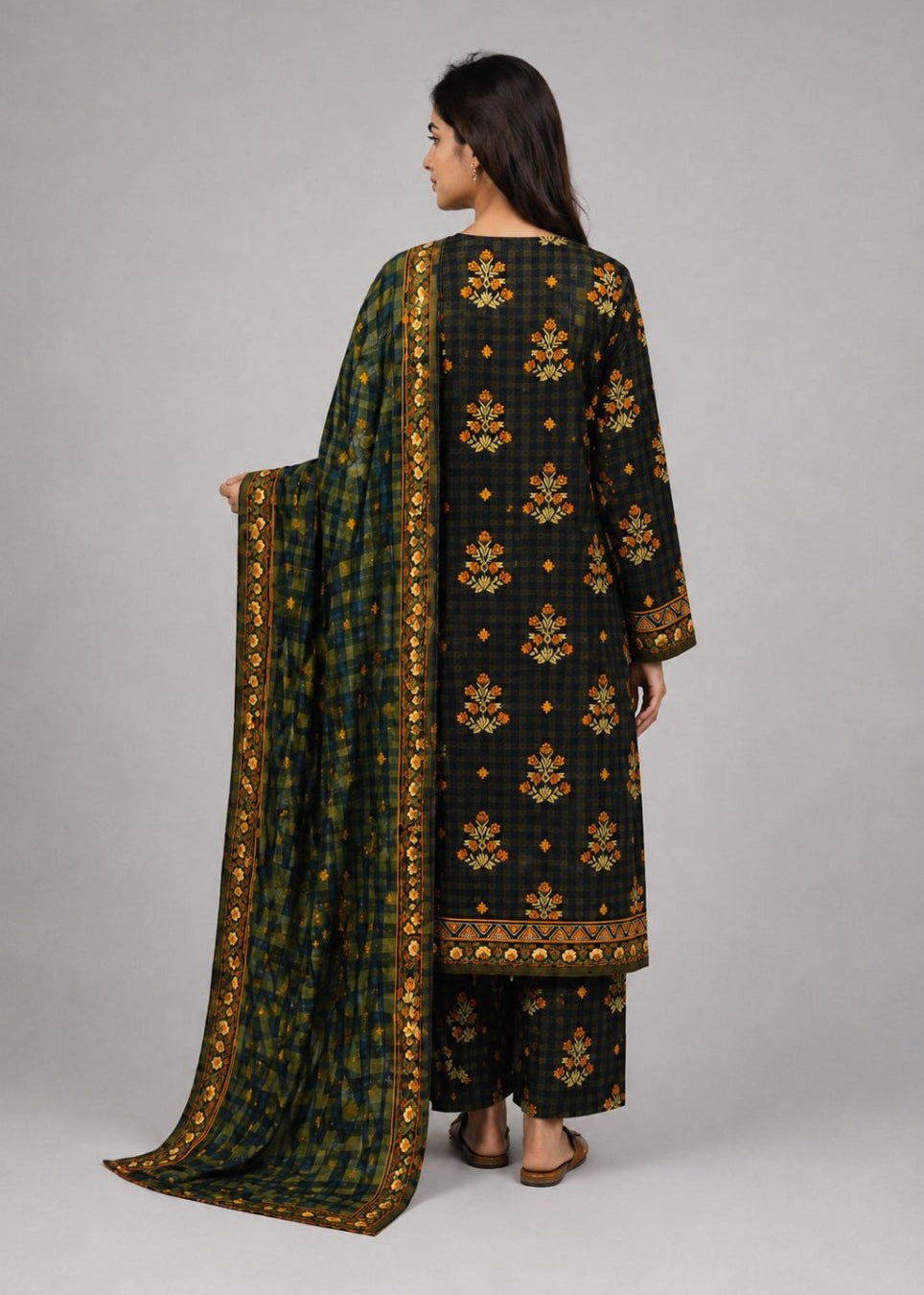 A woman shown from the back wearing a dark green and black traditional outfit with gold floral patterns and holding a matching patterned dupatta, against a neutral gray studio background.