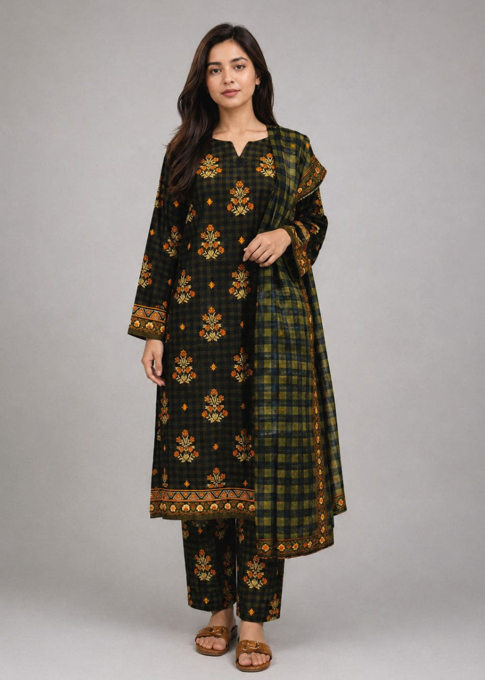 A woman modeling a black and green plaid kurta set with gold floral embroidery and a matching dupatta, photographed against a neutral gray studio background.