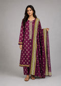 A woman modeling a traditional Indian salwar kameez suit in deep purple with gold and white printed motifs, holding a matching purple dupatta with gold borders against a neutral gray background.
