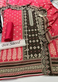 A folded and rolled traditional South Asian salwar suit material set by Bin Saeed, featuring a vibrant pink fabric with gold floral prints, a dark brown base with intricate gold and green geometric embroidery, and a matching pink dupatta.