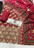 A red traditional South Asian fabric set with intricate gold and multicolor floral embroidery, a matching red fabric piece folded on top, and a white label printed with the brand name 'Bin Saeed'.