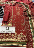 A folded and draped red ethnic fabric set with intricate gold and green floral embroidery and border patterns, featuring a matching rolled fabric piece and a white label reading 'Bin Saeed'.