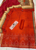 A folded and draped red-orange saree fabric set with a matching red-orange fabric roll and a pink label reading 'Bin Sreed'. The fabric features intricate gold and beige floral patterns along the border and a decorative cutwork border at the bottom, laid out on a white tiled floor.