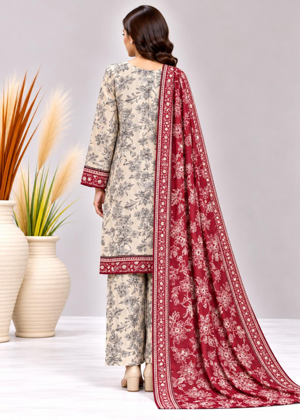 A woman shown from the back wearing a beige printed salwar kameez suit with a deep red border-trimmed kurta, matching trousers, and a long red printed dupatta, photographed against a light gray studio background with decorative vases at the side.