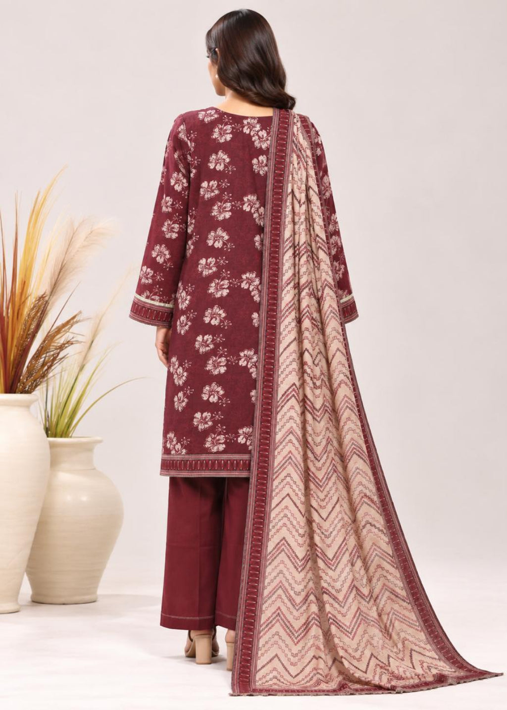 A woman shown from the back wearing a three-piece salwar kameez suit in maroon and beige. The outfit features a maroon printed kurta with beige floral motifs, matching maroon trousers, and a beige and maroon patterned dupatta with chevron designs.