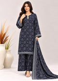 A woman models a navy blue three-piece salwar kameez suit with white geometric prints and border details, including a matching dupatta, set against a light beige studio background with decorative vases.