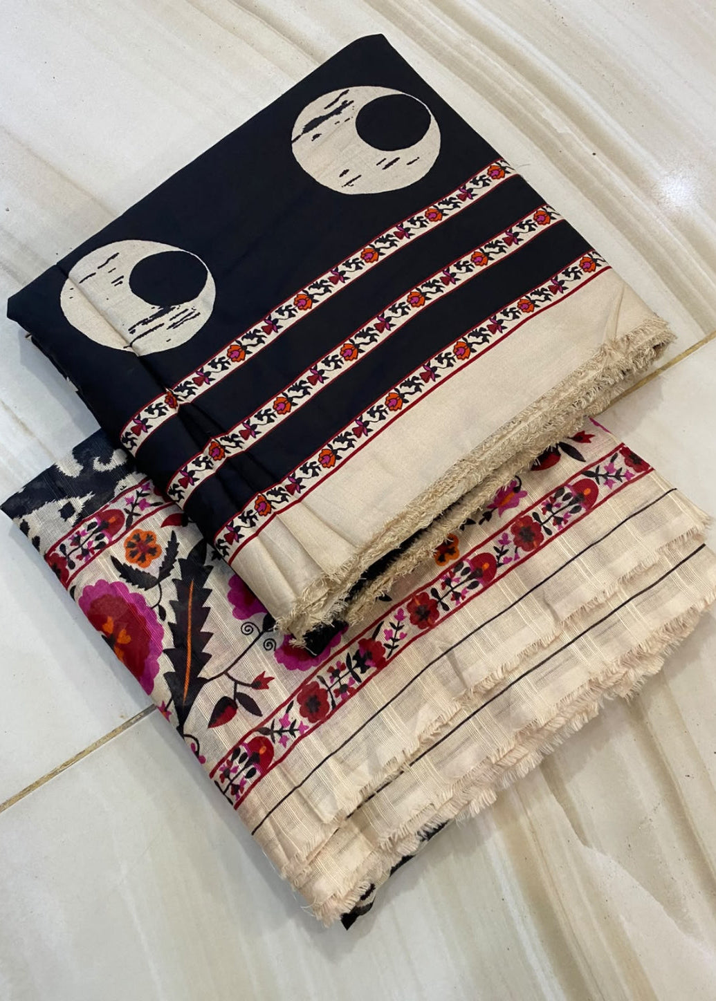 A folded two-piece fabric set, likely a salwar kameez or suit material, featuring a navy blue top with cream crescent moon prints and a beige bottom with colorful floral and geometric patterns, laid flat on a light beige marble tile floor.