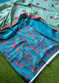 A folded and draped fabric set, likely a sari or scarf, featuring a turquoise blue base with intricate paisley and floral block prints in pink, red, and green, paired with a light mint green border section.