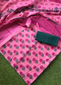 Pink floral printed fabric with a matching striped border and a folded dark green fabric piece placed on top, laid out on green grass.
