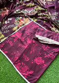 A draped piece of deep magenta-purple fabric with a pink floral print and white border trim, laid out on green artificial grass. A folded matching fabric piece with a lace trim is placed on top.