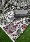 A folded and unfolded piece of printed fabric laid on artificial green grass. The fabric has a white base with gray and black paisley and floral motifs, plus bright pink floral accents, with a folded gray fabric piece placed on top.