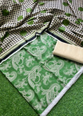 A green and white printed fabric set laid out on artificial grass, featuring a paisley patterned main section, a black-and-white dotted dupatta, and a folded beige fabric piece.