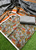 A folded and draped saree fabric set on artificial green grass, featuring a gray base with a colorful floral and paisley print in orange, red, yellow, and green, along with a matching gray fabric roll.