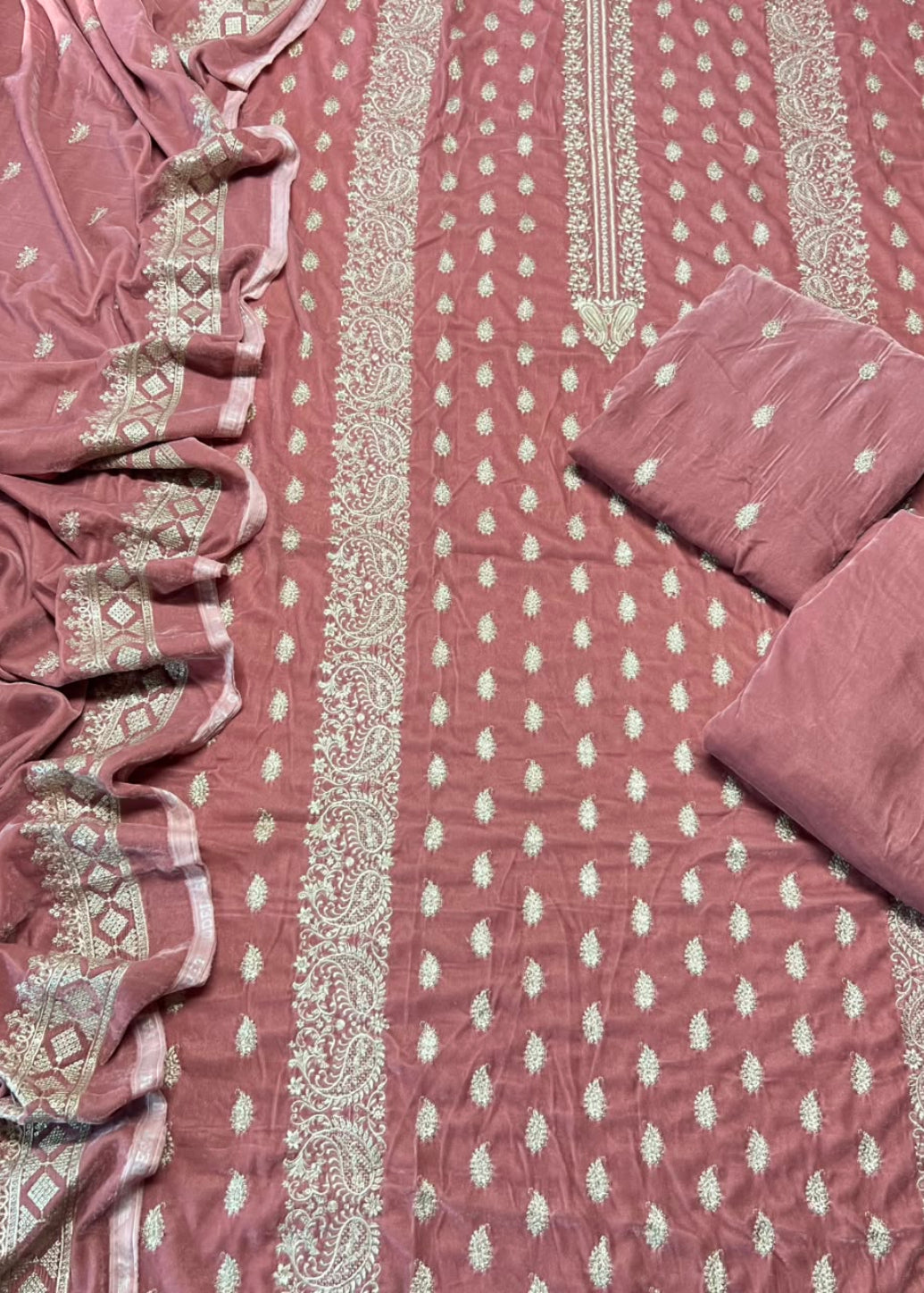 A dusty rose pink fabric set with intricate beige and gold zari embroidery, featuring a main fabric panel with vertical borders, a matching dupatta draped on the left, and two folded fabric pieces on the right.