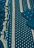 A close-up of a teal blue fabric textile with white embroidered patterns, borders, and matching folded fabric pieces arranged on the right side.