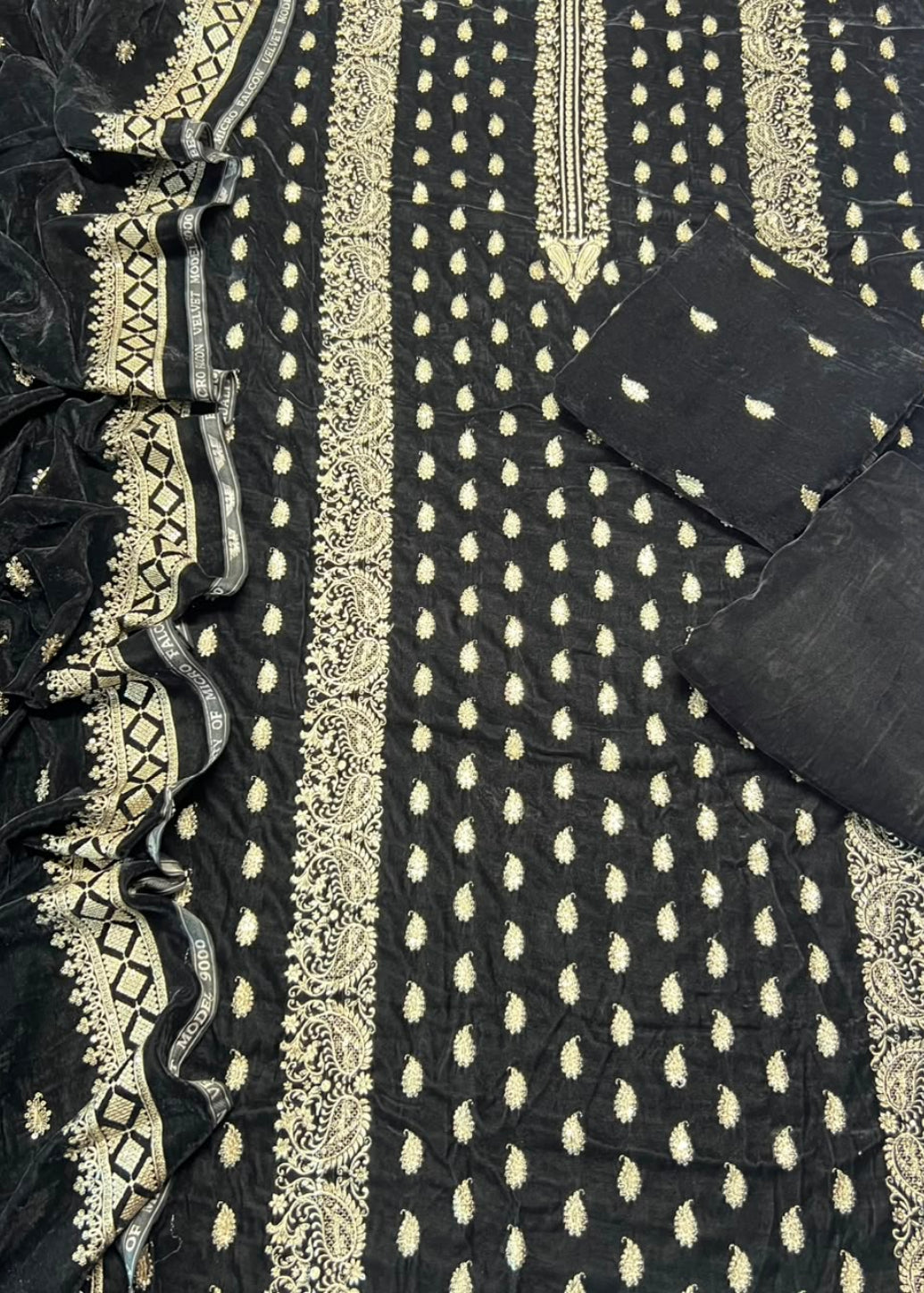 Black cotton fabric salwar suit material with beige embroidery, featuring a printed body with small teardrop motifs, a decorative border, matching dupatta, and two fabric pockets.