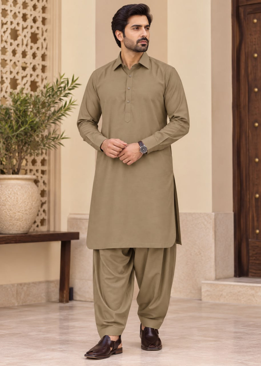 A man modeling a traditional Indian outfit consisting of a long-sleeve kurta and matching pants in a warm khaki or olive-brown color, standing in an indoor architectural setting.