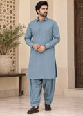 A man modeling a light blue traditional shirtdhoti set with matching pants, standing in a courtyard setting.