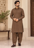 A man modeling a brown long-sleeve kurta and matching pants set in a traditional indoor setting with beige walls and a wooden door.