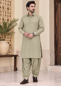 A man modeling a light sage green traditional South Asian outfit consisting of a long-sleeve kurta and matching pants, standing in a decorated indoor setting.