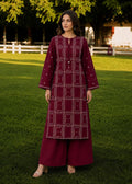 A woman stands on a green lawn wearing a deep maroon embroidered kurta with matching wide-leg trousers. The kurta features white geometric patterns and a central embroidered panel, paired with a matching maroon tunic underneath.