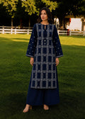 A woman stands on a green lawn wearing a navy blue embroidered kurta with wide sleeves and matching wide-leg pants. The outfit features white geometric embroidery and small white dot details.