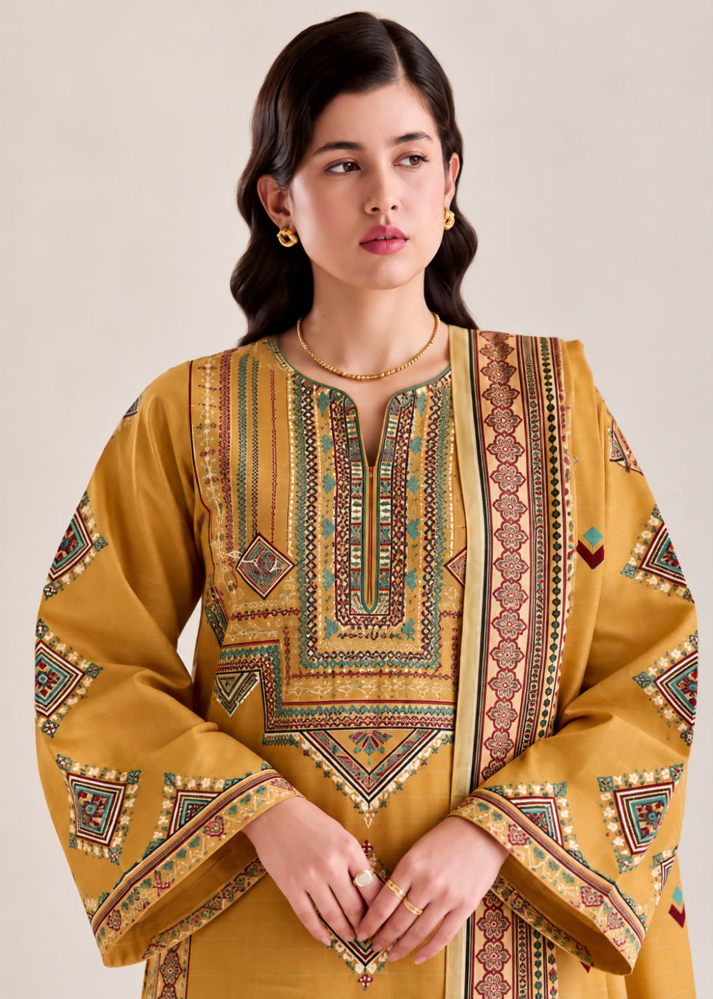 A woman wearing a mustard yellow kurta with intricate multicolor geometric and tribal patterns, set against a plain beige background.