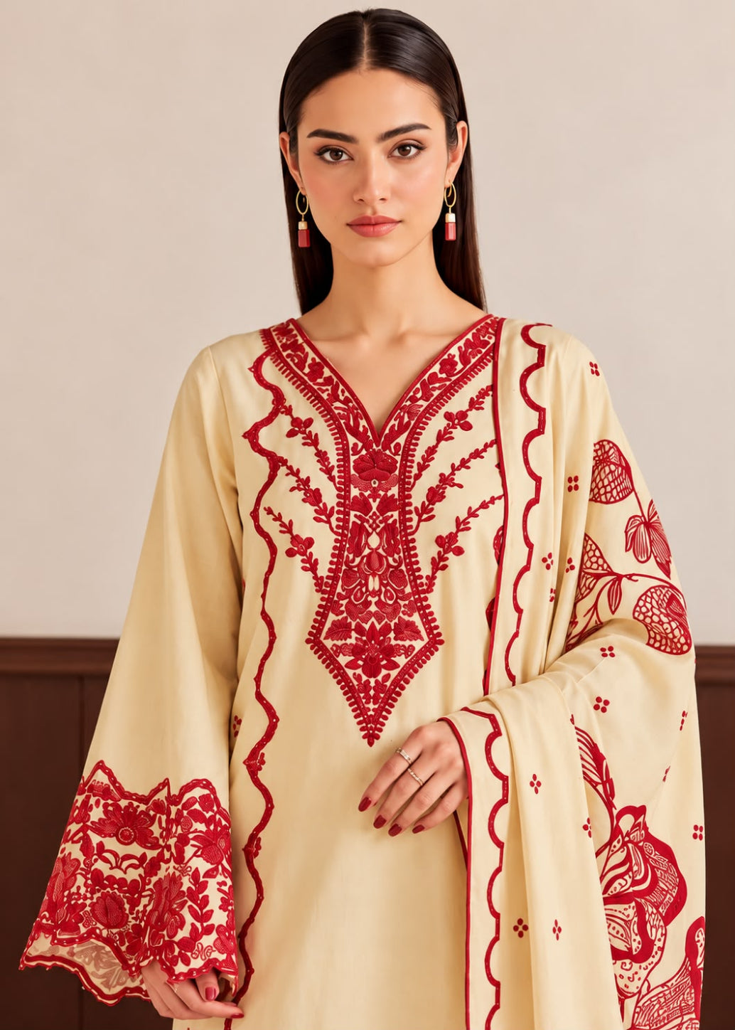 A woman wearing a cream-colored traditional tunic with vibrant red embroidery, featuring a V-neckline, ornate chest detailing, and patterned sleeves, set against a neutral indoor background.