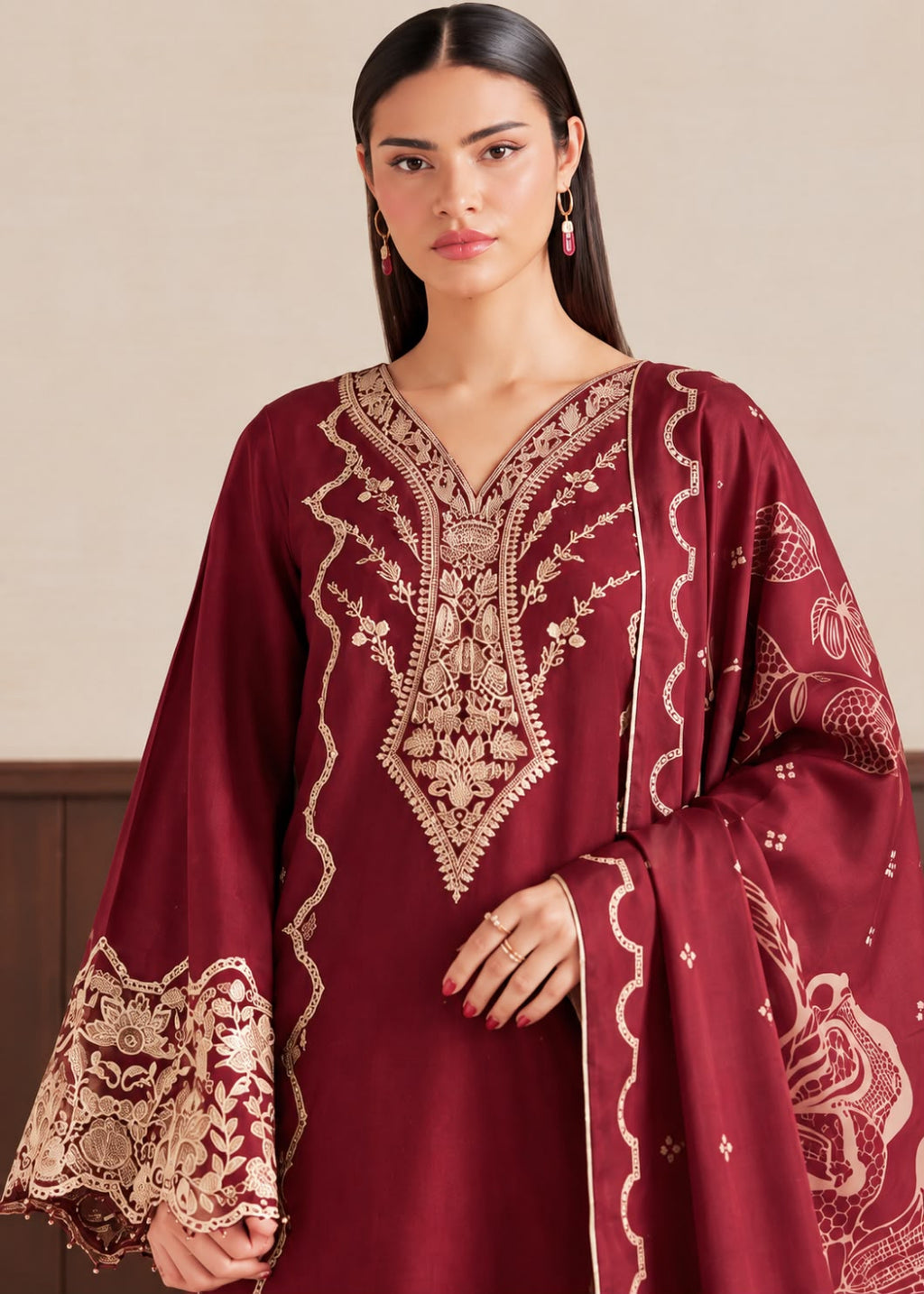 A woman modeling a deep maroon traditional kurta with intricate gold embroidery on the neckline, sleeves, and cuffs, set against a neutral beige background.