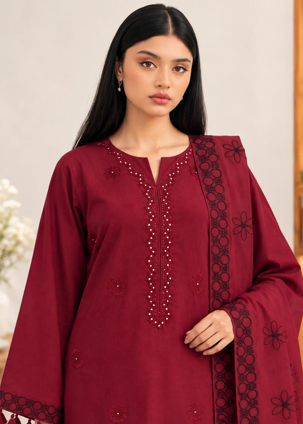 A woman modeling a deep maroon kurta with black floral embroidery and beadwork details, paired with a matching dupatta, set against a soft beige background.