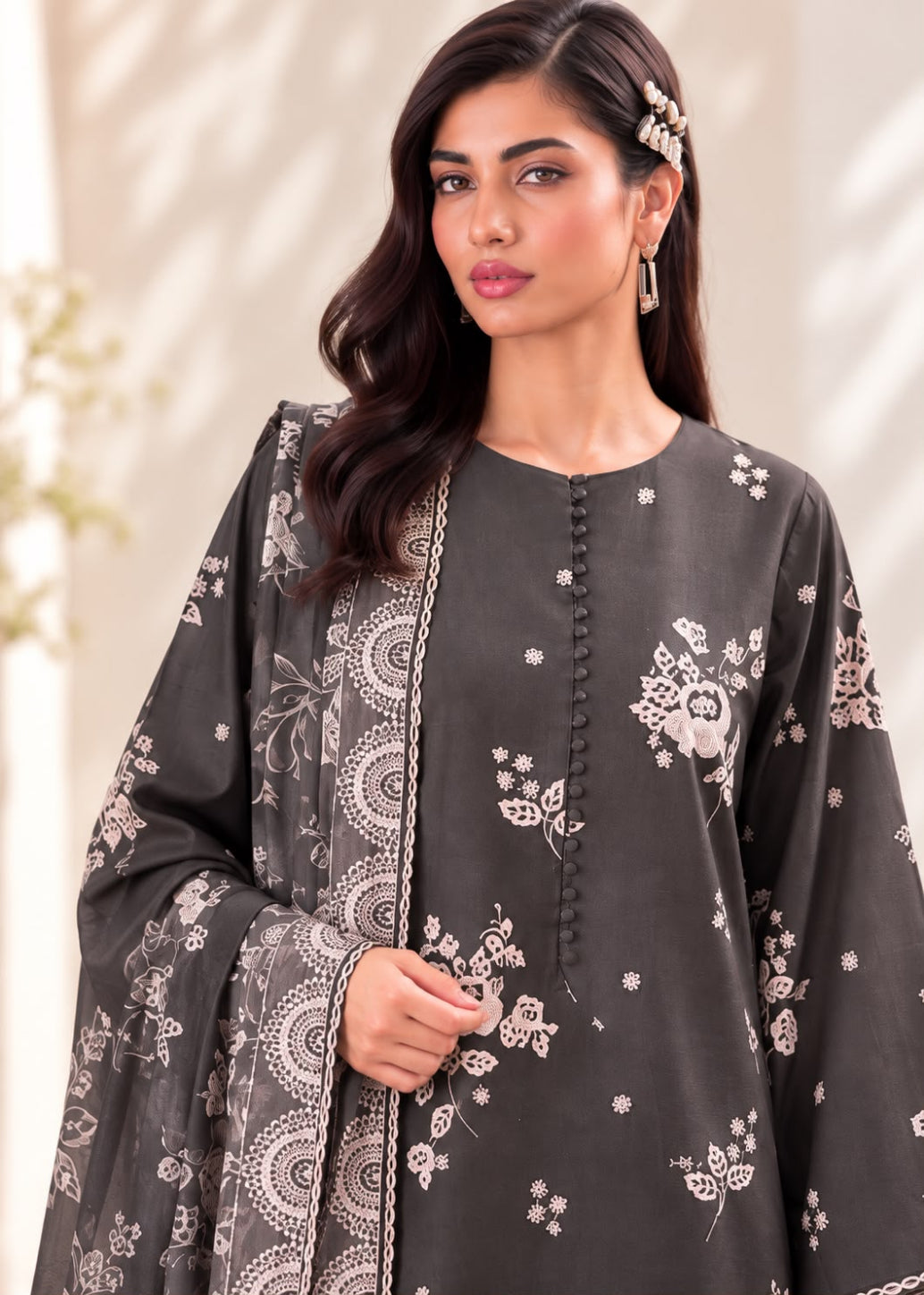 A woman modeling a dark gray traditional outfit with white floral and paisley patterns, featuring a round neckline, front button placket, and matching dupatta.