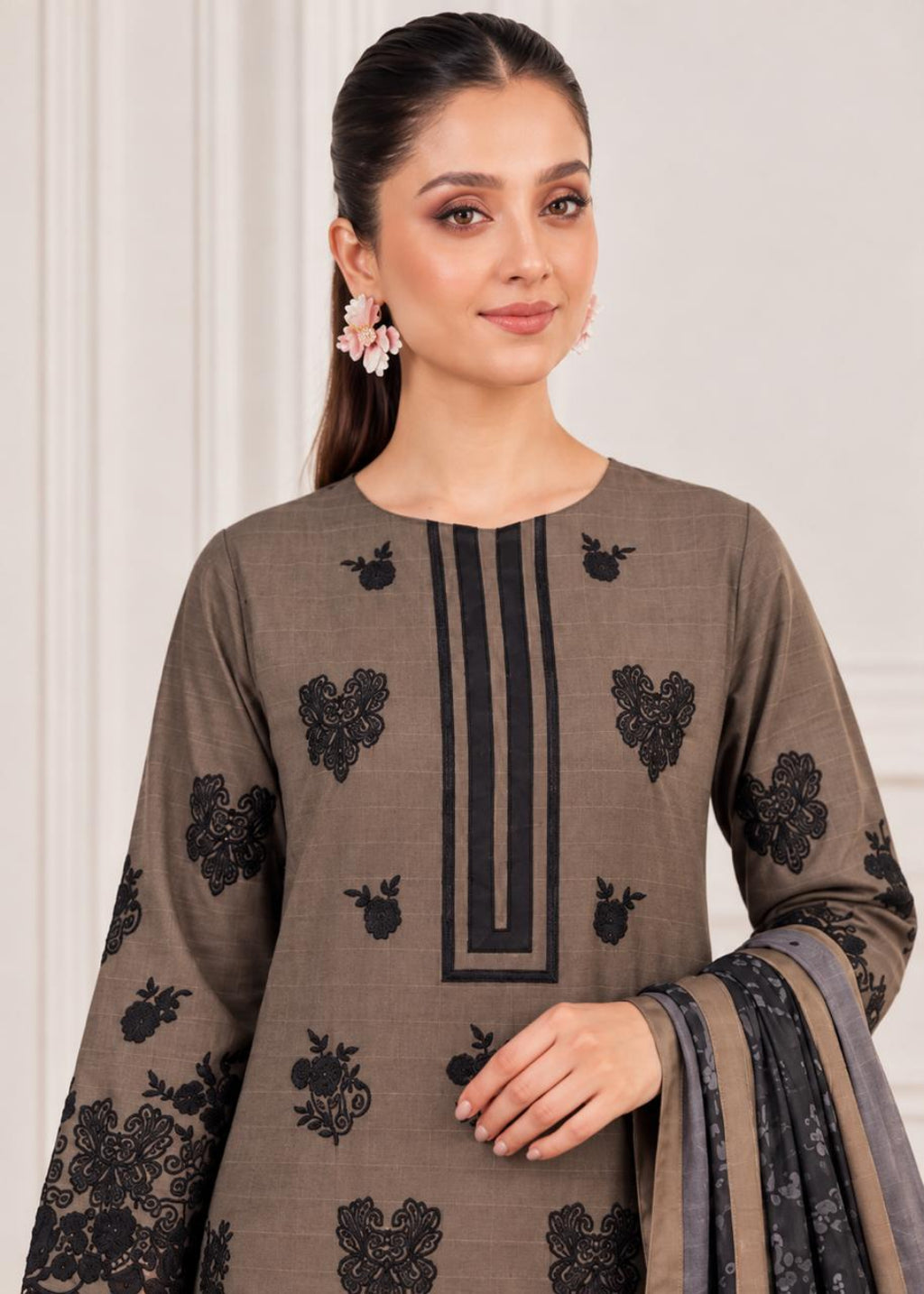 A woman wearing a taupe-brown traditional kurta with black floral embroidery and a vertical black stripe detail on the chest, paired with a matching dupatta, set against a neutral indoor background.