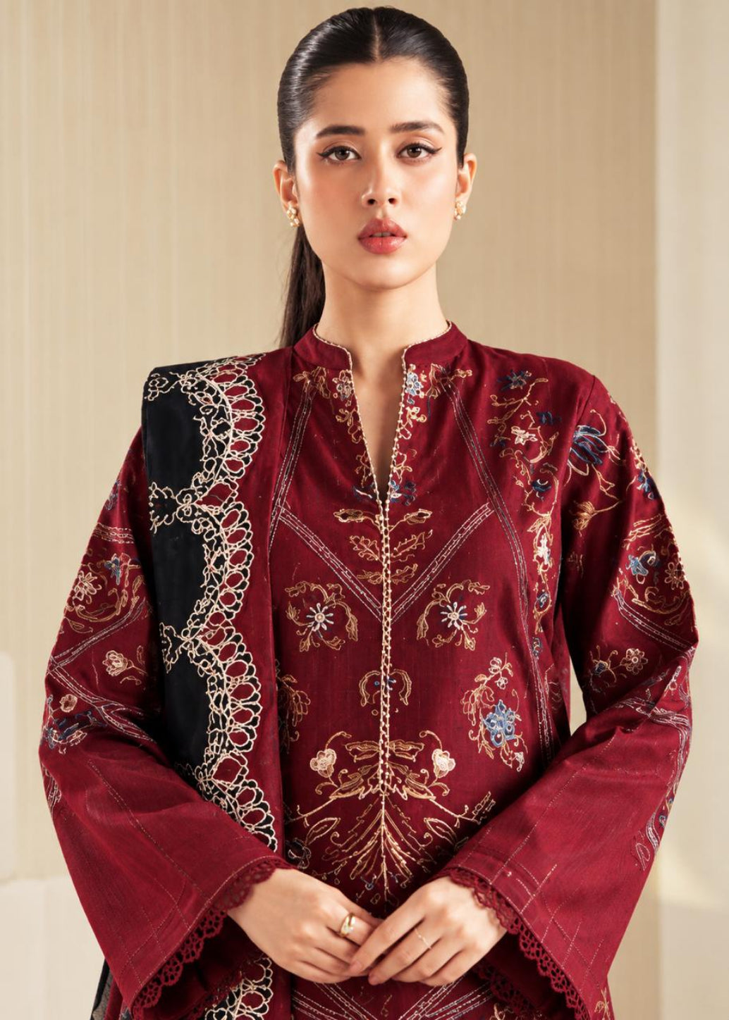 A woman modeling a deep maroon embroidered kurta with a matching maroon dupatta featuring a black border and intricate gold, blue, and white embroidery.